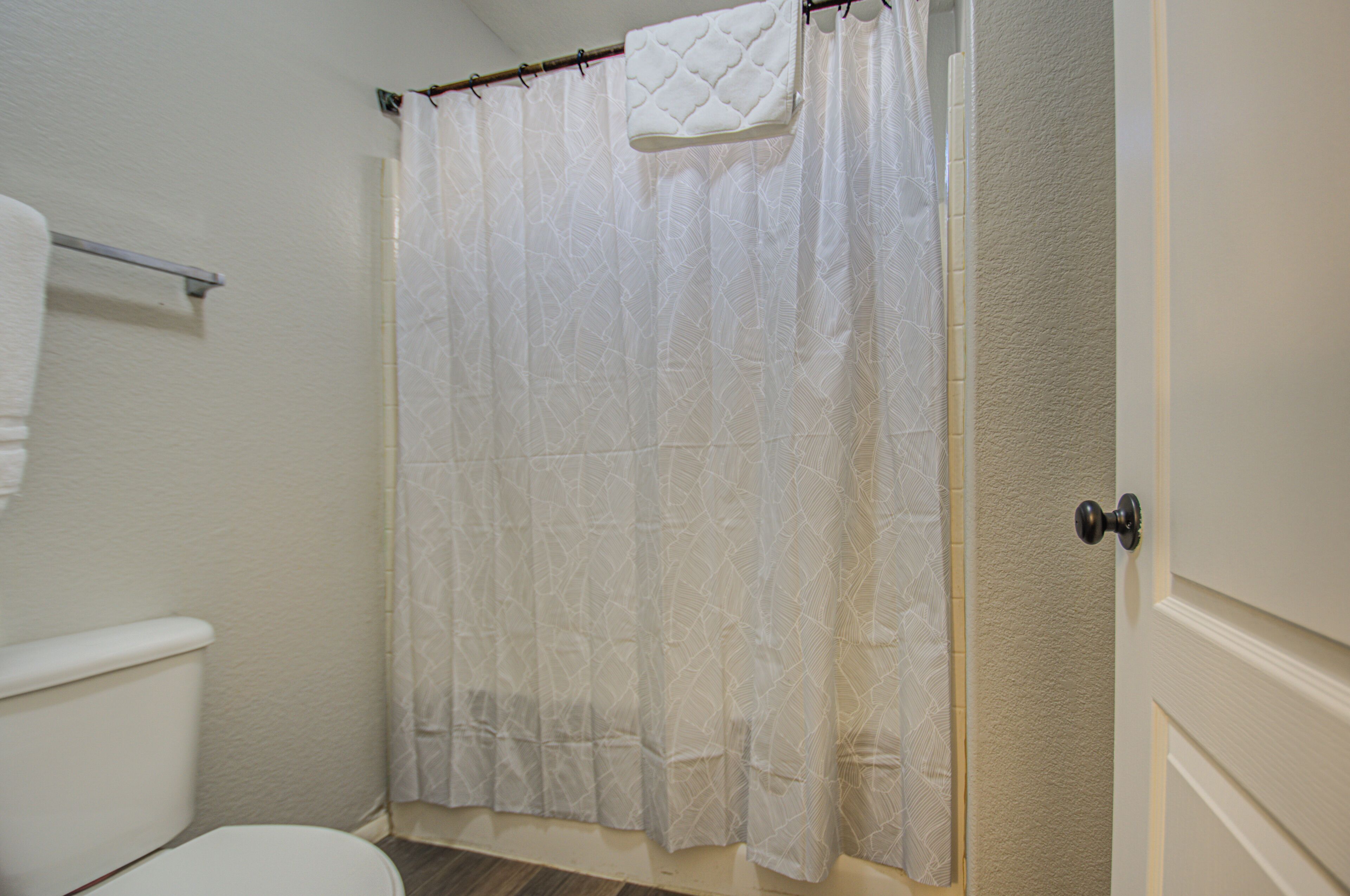 Un baño con inodoro blanco, cortina de ducha y toallero.
