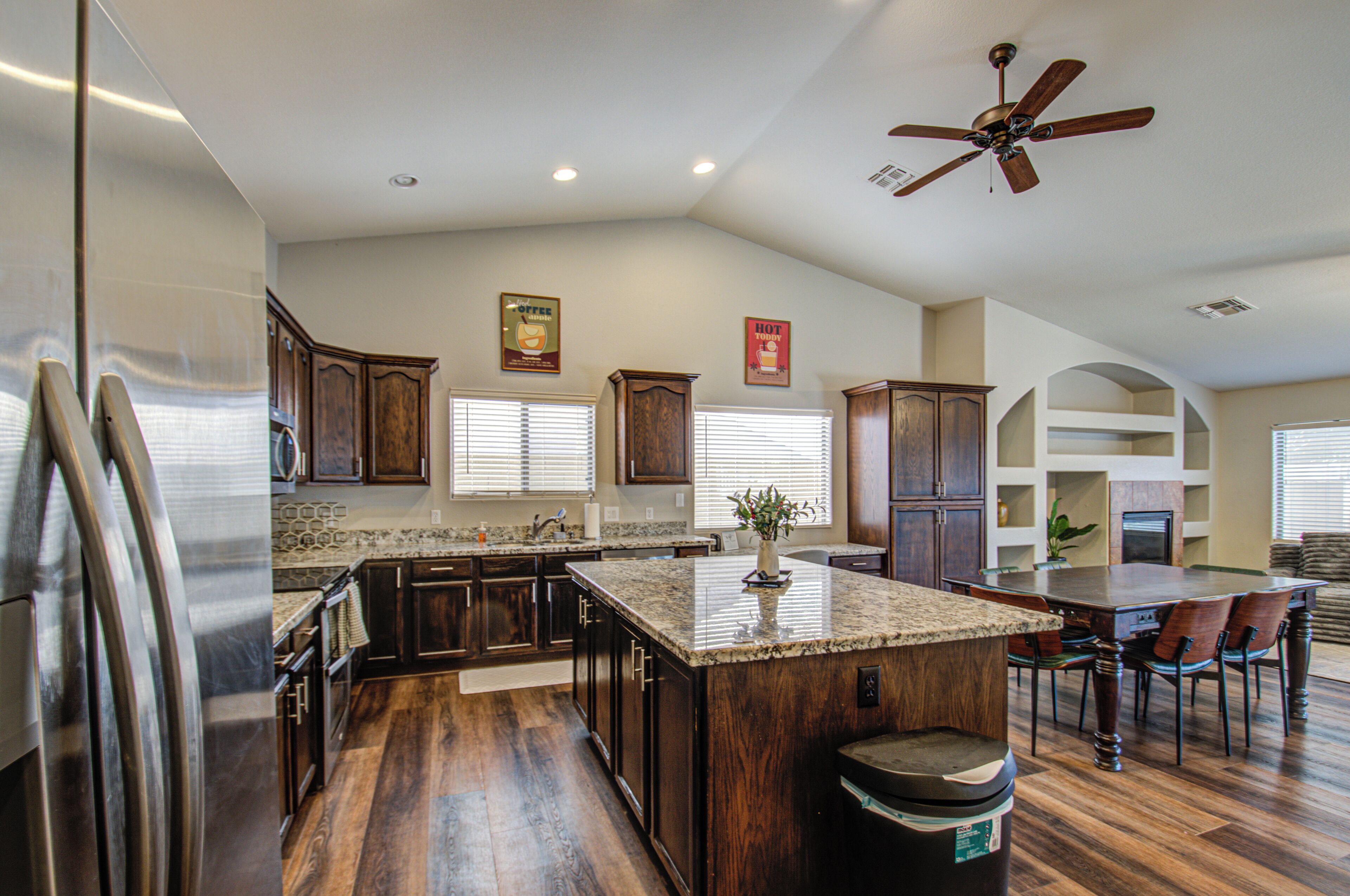 A spacious kitchen with dark wood cabinets, a granite countertop island, and a ceiling fan.