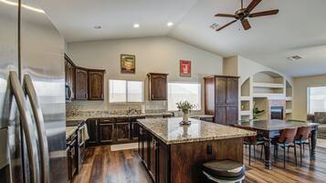 A spacious kitchen with dark wood cabinets, a granite countertop island, and a ceiling fan.