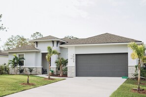 A modern two-story house with a grey garage door, a small front yard with palm trees, and a clear sky. - SPACIOUS family house, North Port with POOL/ SPA, SECLUDED (North Port)