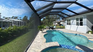 A swimming pool with a glass enclosure, surrounded by a landscaped area with a lawn and a house in the background.