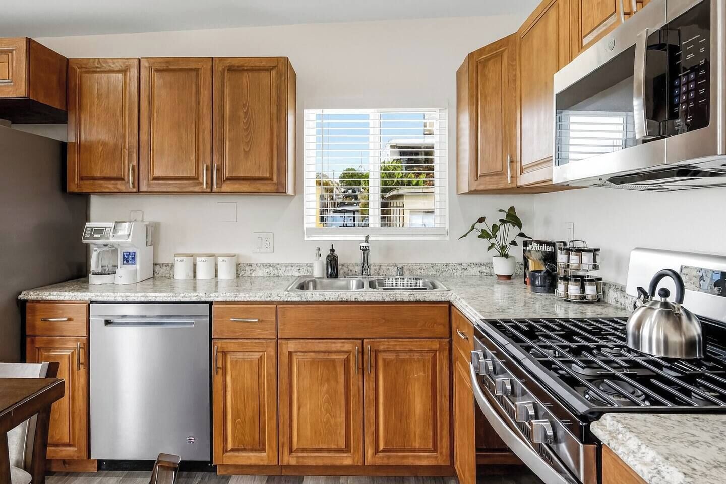 A kitchen with wooden cabinets, a stainless steel dishwasher, a gas stove, and a window with blinds.