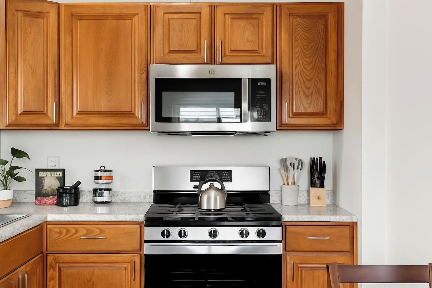 Una cucina con mobili in legno, un forno a microonde in acciaio inossidabile, un fornello e diversi utensili da cucina.