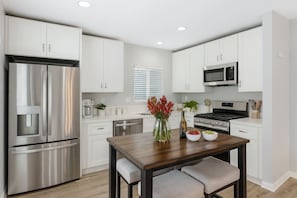 A modern kitchen with white cabinets, stainless steel appliances, and a wooden dining table. - Leyla| Pool/Spa|Downtown|Freeways|Beaches (San Diego)
