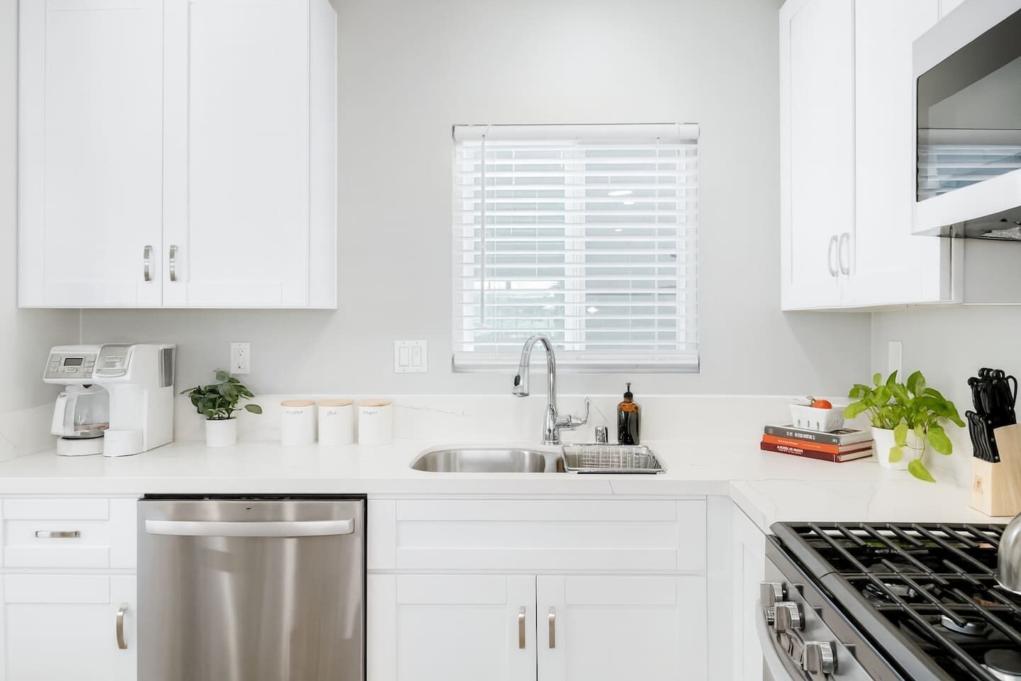 Una cocina moderna con armarios blancos, lavavajillas de acero inoxidable, un fregadero, una estufa y una ventana con persianas.
