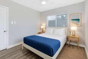 A bedroom with a bed, two bedside tables, a window with blinds, a ceiling fan, and a framed picture on the wall. - Leyla| Pool/Spa|Downtown|Freeways|Beaches (San Diego)