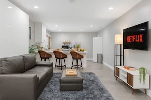 A modern living room with a sofa, a coffee table, and a TV mounted on the wall displaying 'NETFLIX'. - Three Private Units| Pool/Spa|Downtown|Freeways|Beaches (San Diego)