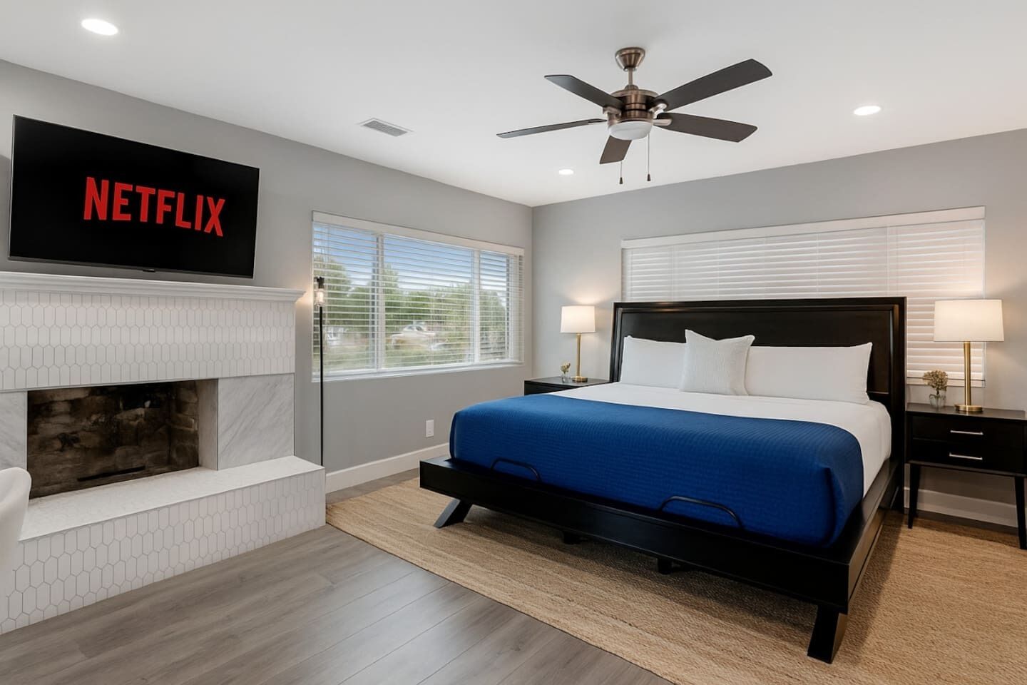 Un dormitorio moderno con una cama, una chimenea, un ventilador de techo y un televisor que muestra 'NETFLIX'.