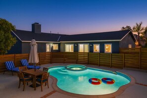 Ein Garten mit Schwimmbad, einer Holzterrasse und einem Essbereich mit Stühlen und Tisch.