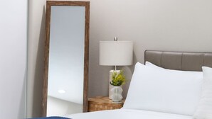 A hotel room with a bed, a nightstand with a lamp and a vase of flowers, and a large mirror.