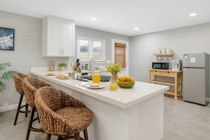 Una cocina moderna con una isla central, taburetes de bar, un refrigerador y un microondas.