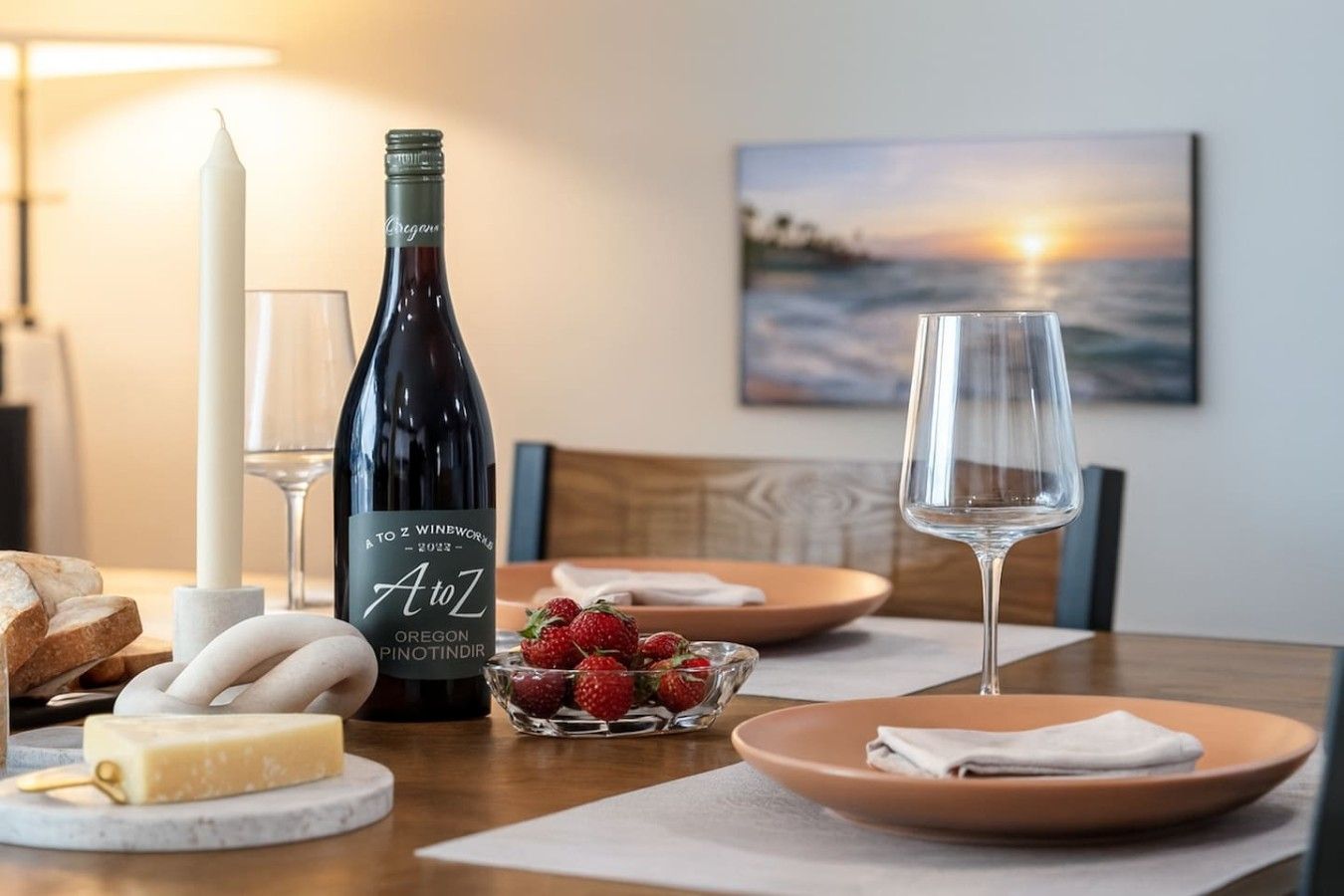A dining table with a bottle of wine, glasses, cheese, strawberries, and bread.