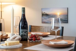 Una mesa de comedor con una botella de vino, copas, queso, fresas y pan.