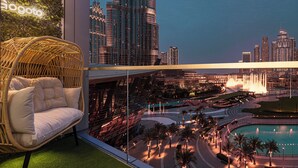 A balcony with a wicker sofa, a cityscape view, and a fountain. - GOGOTO Burj & Fountain View Stay (Dubai)