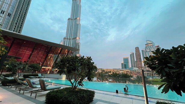 A pool area with lounge chairs, a glass barrier, and a view of tall buildings in the background. - GOGOTO Burj & Fountain View Stay (Dubai)