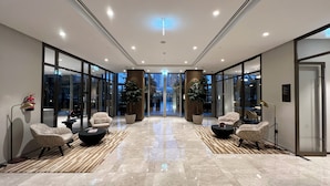 A modern hotel lobby with a glass entrance, seating area with armchairs and a coffee table, and a fire extinguisher on the wall. - GOGOTO Burj & Fountain View Stay (Dubai)