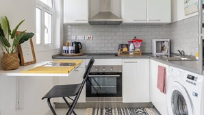 Una cocina compacta con armarios blancos, un horno de acero inoxidable, lavadora integrada y un ventanal que proporciona luz natural.