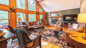 A cozy living room with a stone fireplace, large windows, and a television.