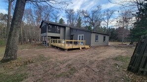 A two-story house with a deck, surrounded by trees and a dirt yard. -  Newly listed: Ray's Retreat  (Webster)