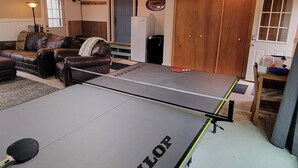 A ping pong table with 'DUNLOP' branding, a leather sofa, a lamp, and a door with a 'WELCOME' sign. -  Newly listed: Ray's Retreat  (Webster)