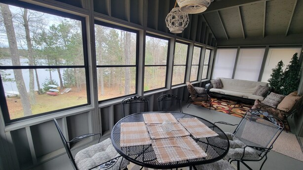 A covered patio with a table and chairs, a sofa, and a view of trees and a lake. -  Newly listed: Ray's Retreat  (Webster)