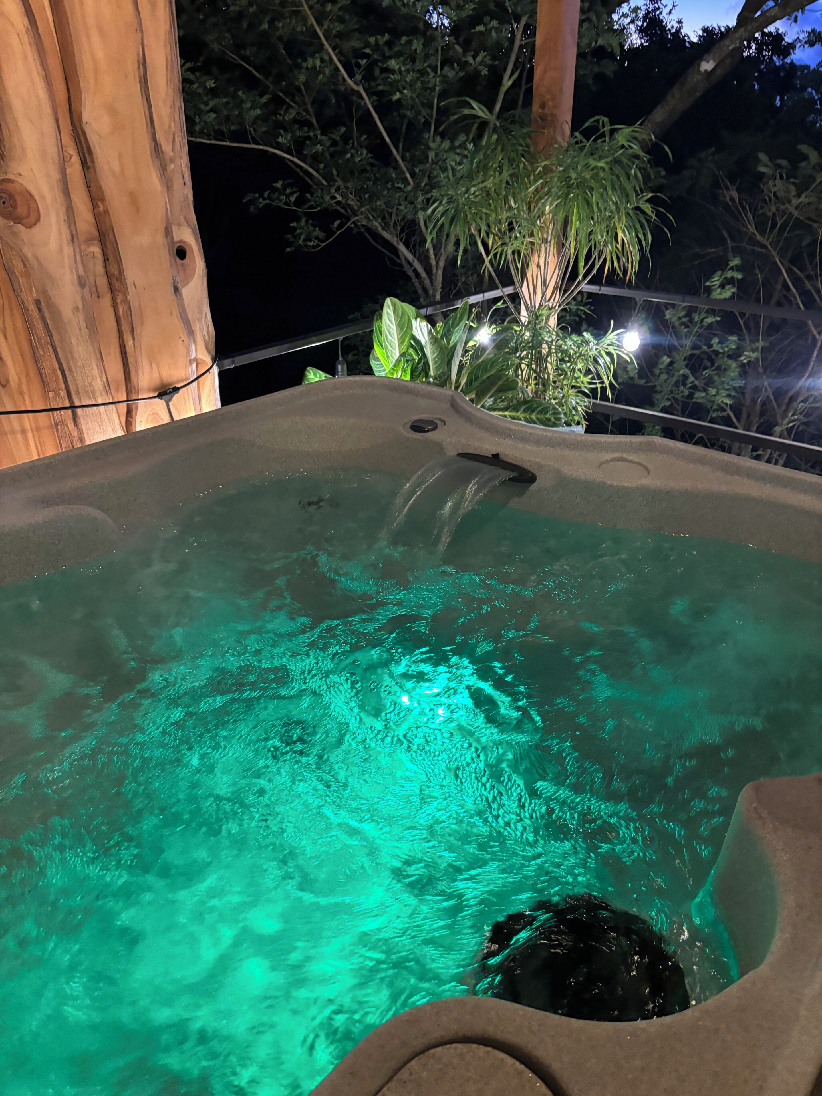Uma banheira de hidromassagem com água cristalina, rodeada por árvores e uma estrutura de madeira.