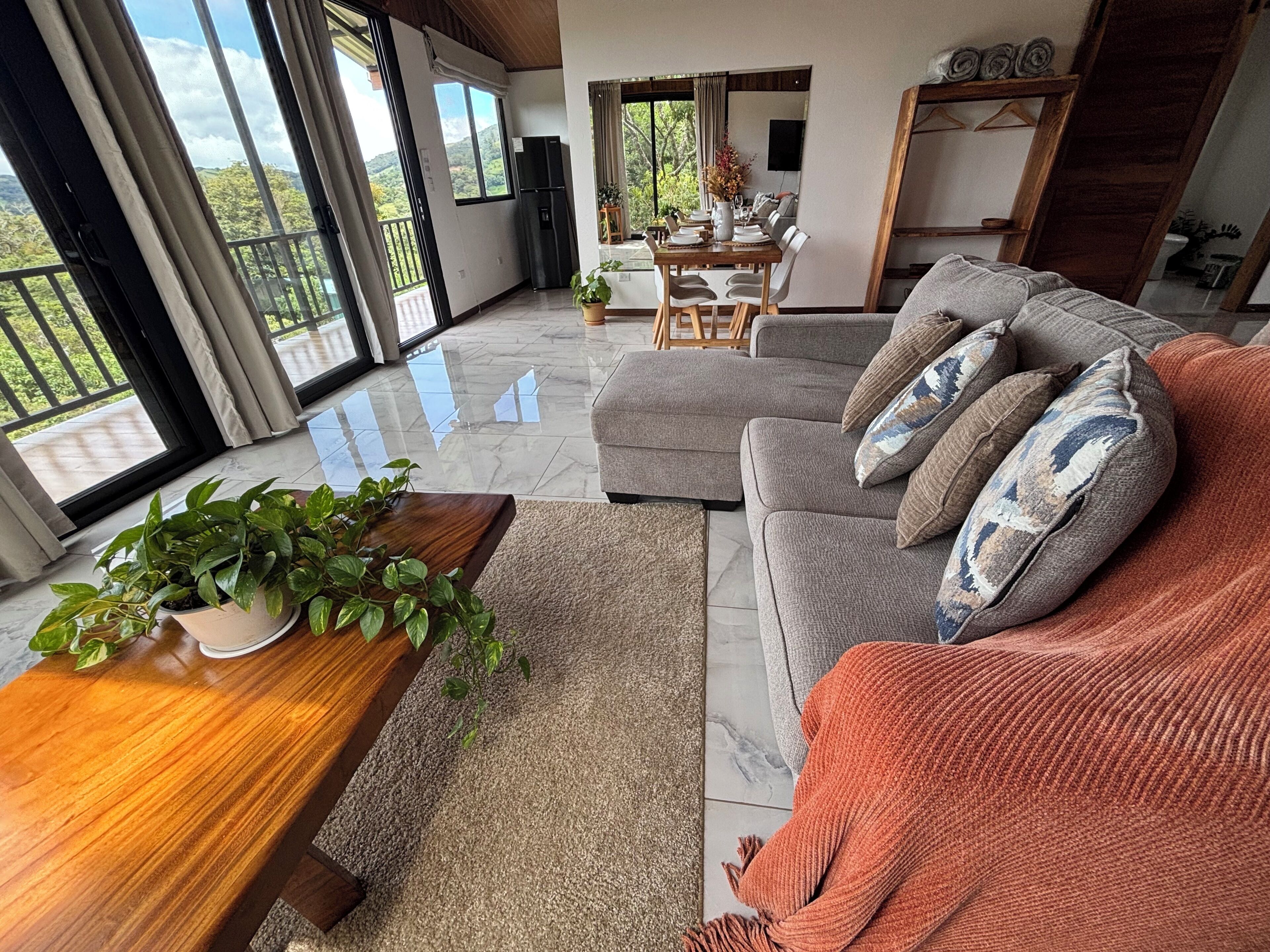 Una sala de estar moderna con un sofá, una mesa de centro con plantas y un comedor con mesa dispuesta para cuatro.