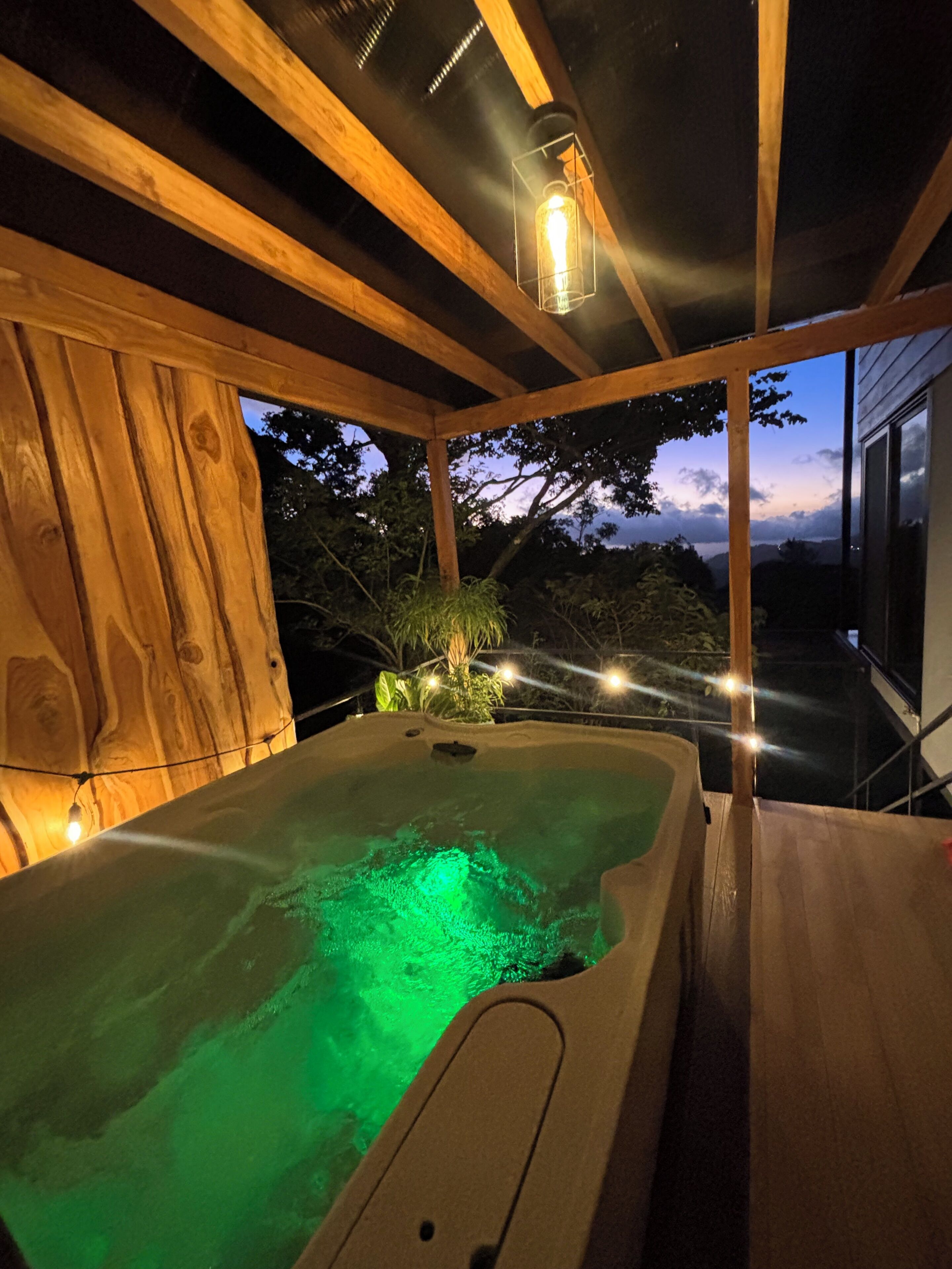 Un bain à remous avec un éclairage vert, des poutres en bois et une vue sur le ciel.