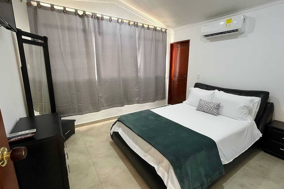 Een slaapkamer met een bed, nachtkastjes, een kledingkast, een raam met gordijnen en een airconditioner.