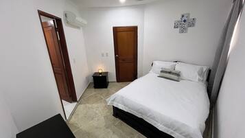 Un dormitorio con cama, mesita de noche, aire acondicionado instalado en la pared y una puerta.