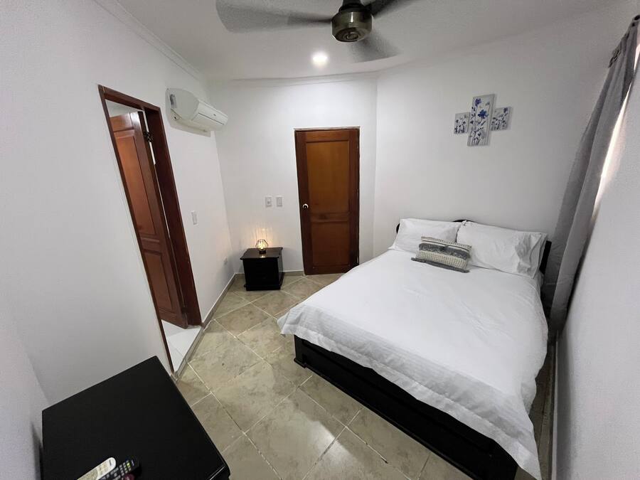 Un dormitorio con cama, mesita de noche, aire acondicionado instalado en la pared y una puerta.