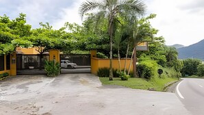 A residential driveway with a gated entrance, a parked vehicle, and lush greenery. - Linda casa em Boiçucanga (Sao Sebastiao)