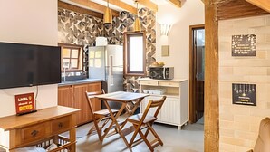 A compact kitchen with a dining area, wooden beams, a TV, and a refrigerator. - Linda casa em Boiçucanga (Sao Sebastiao)
