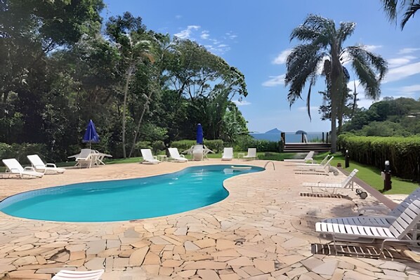 A pool area with lounge chairs and a view of the ocean. - Linda casa em Boiçucanga (Sao Sebastiao)