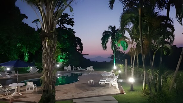 A pool area with lounge chairs and umbrellas, surrounded by palm trees and a sunset view. - Linda casa em Boiçucanga (Sao Sebastiao)