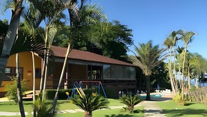 A building with a red roof and large windows, surrounded by lush greenery and palm trees. - Linda casa em Boiçucanga (Sao Sebastiao)