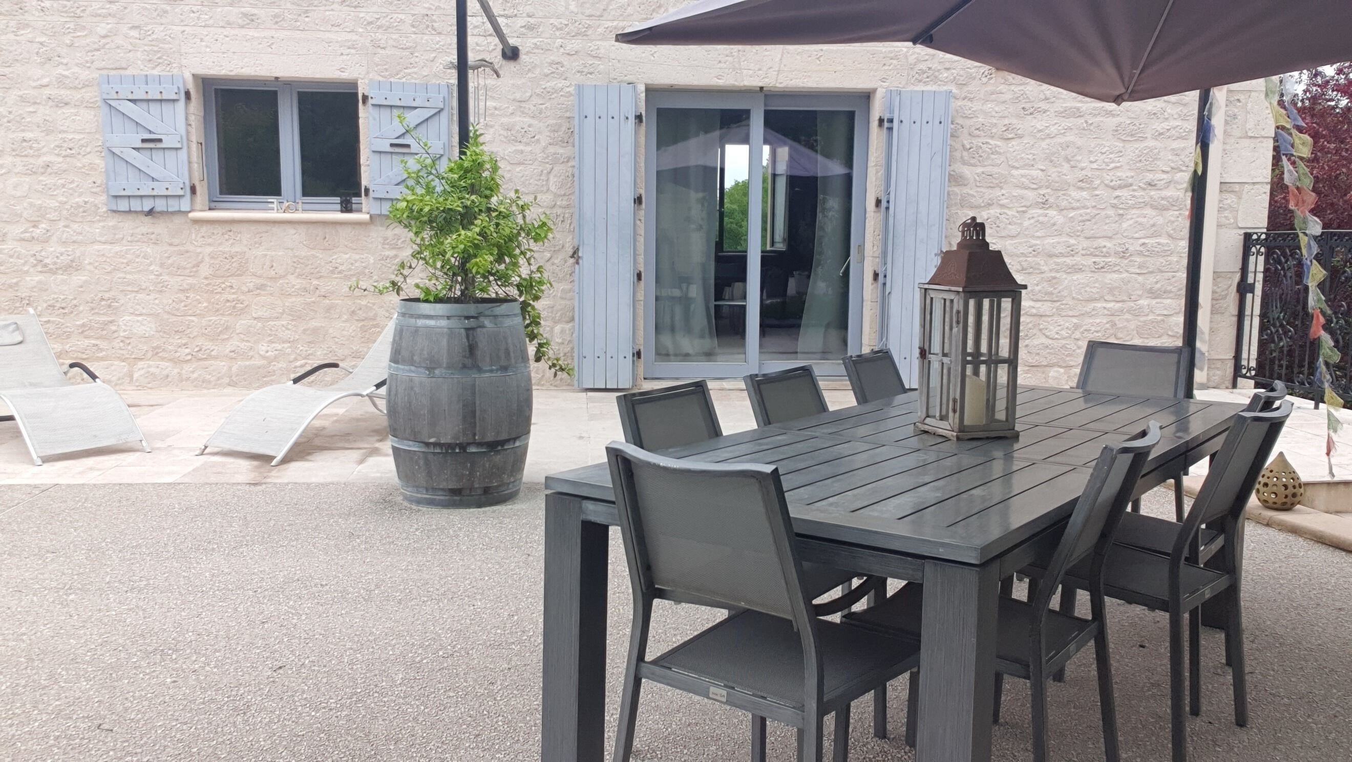 Un patio al aire libre con una mesa y sillas de madera, una planta en maceta y un farol.