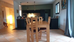 Une cuisine moderne avec des meubles de couleur sombre, une table à manger entourée de chaises en bois et un sol carrelé.