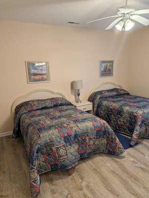 A bedroom with two beds, a ceiling fan, and two wall-mounted lamps.
