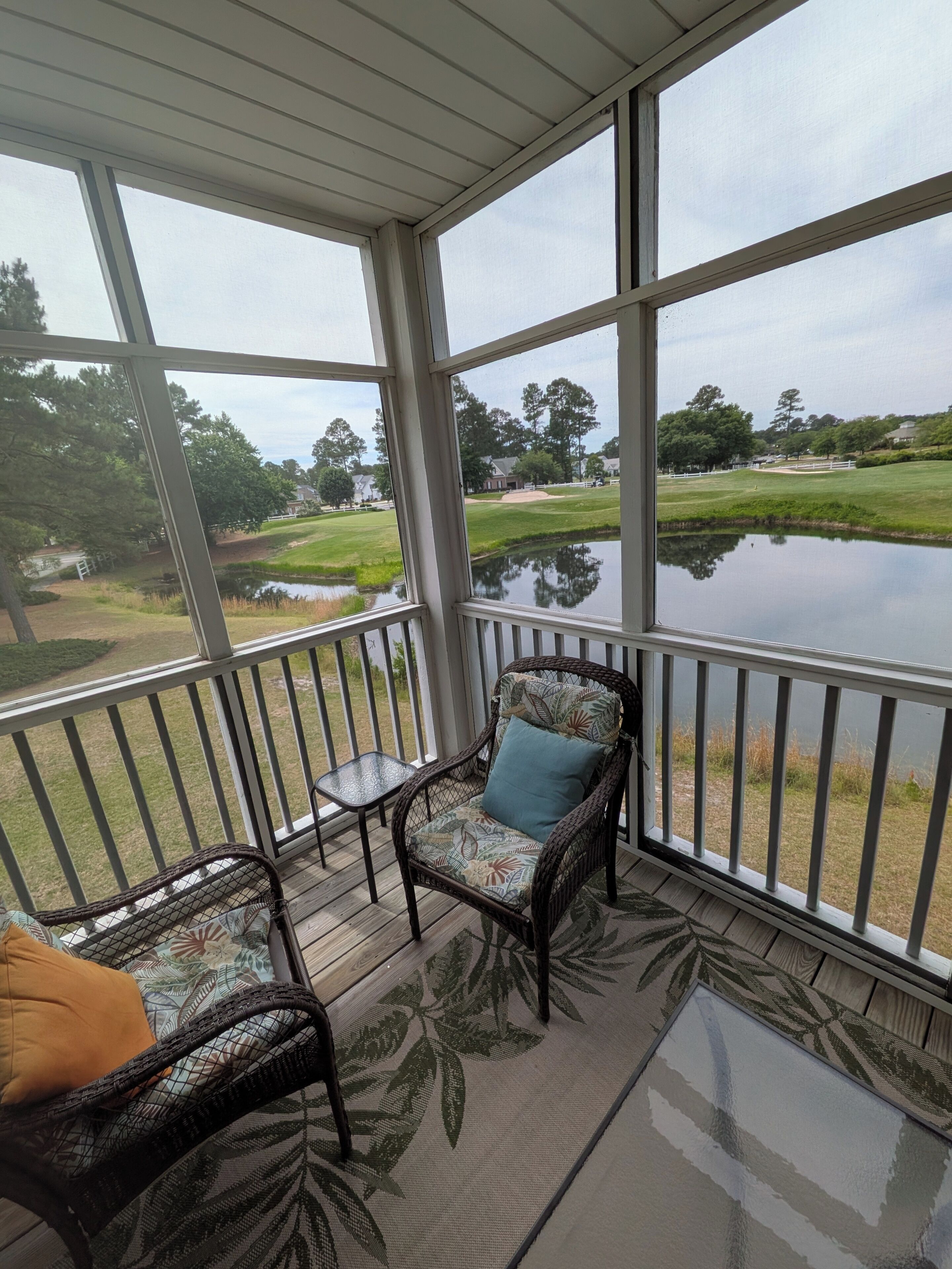 A covered outdoor area with wicker furniture and a view of a golf course and pond.