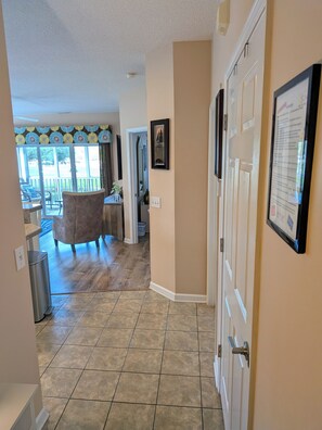 Un pasillo que conduce a una sala de estar con vista al exterior, una puerta con un marco de fotos y un basurero.