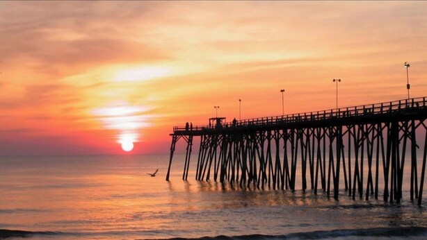 A pier extending into the water with a sunset in the background.