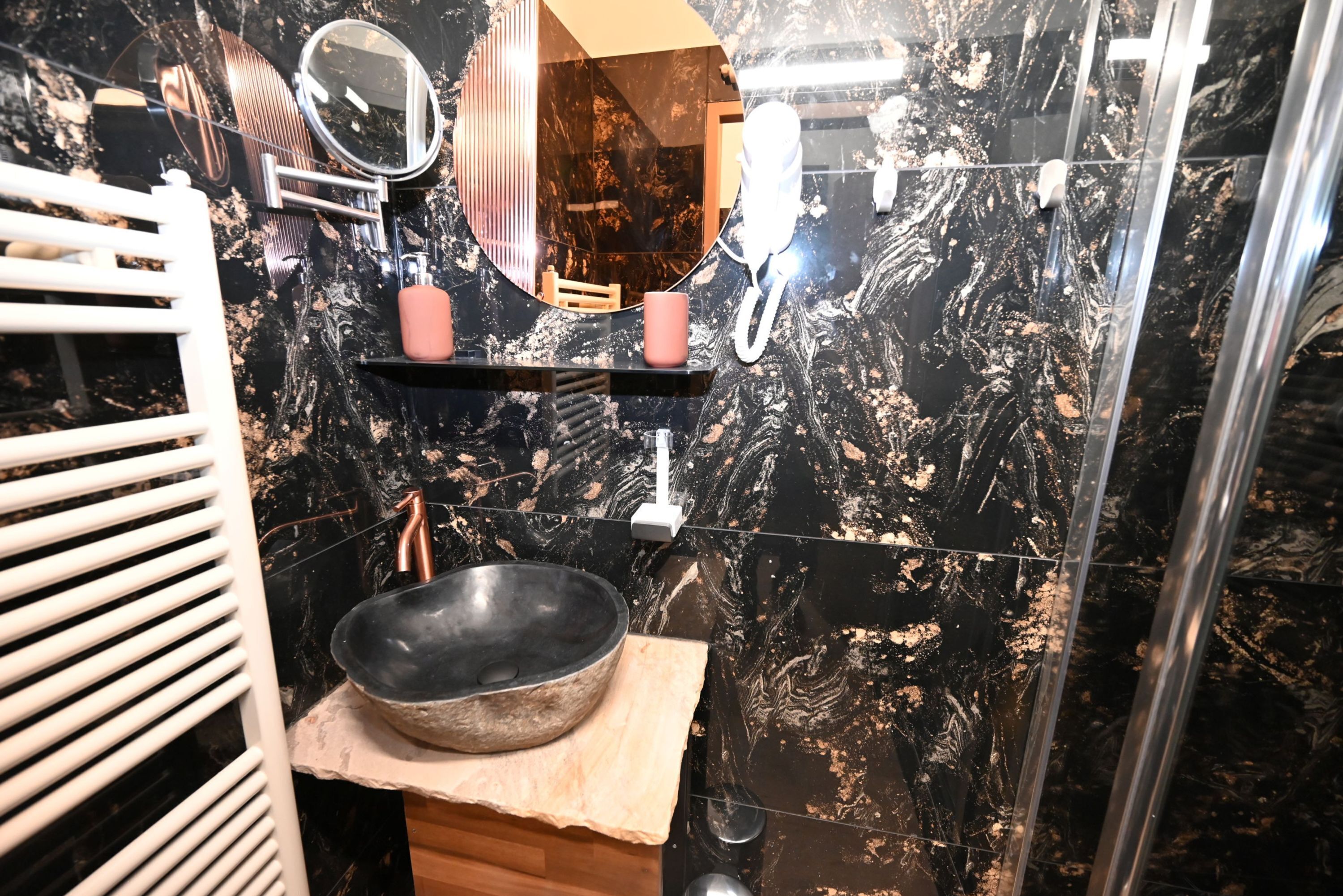 Un baño con lavamanos de mármol negro, un espejo y un perchero para toallas.