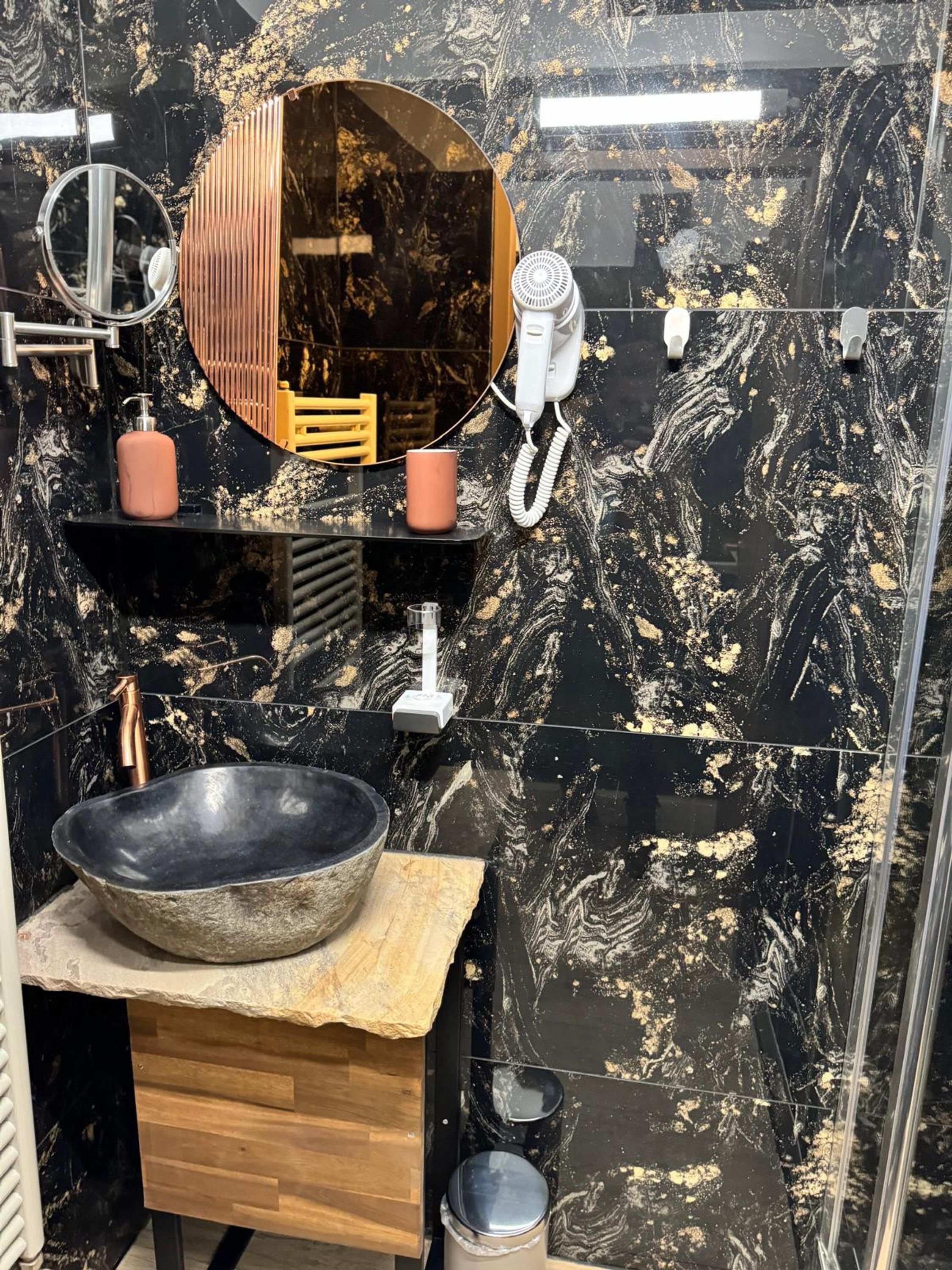 Un baño moderno con un lavamanos de mármol negro, un mueble de tocador de madera, un espejo grande y un secador de pelo.