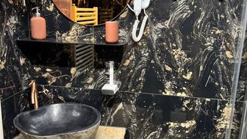 Un baño moderno con un lavamanos de mármol negro, un mueble de tocador de madera, un espejo grande y un secador de pelo.