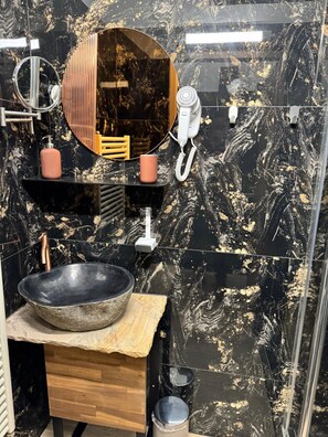 A modern bathroom with a black marble sink, a wooden vanity, a large mirror, and a hairdryer.