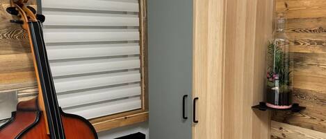 A room with a wooden floor, a large cabinet, a violin, and a window with blinds.