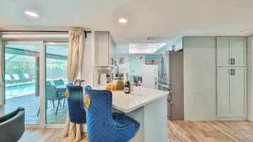 A modern kitchen with a large island, a dining area with blue chairs, and a view of a pool through a glass door.
