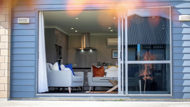 Une maison moderne dotée d’une porte-fenêtre coulissante qui donne sur un espace de vie comprenant deux canapés et une table basse.