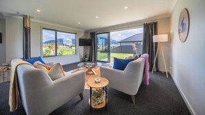 Un salon moderne avec deux canapés, une table basse et un téléviseur. De grandes fenêtres offrent une vue sur l’extérieur.